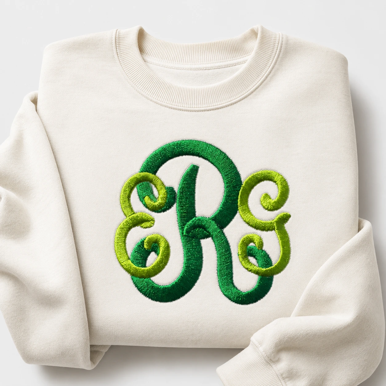 Classic green monogram embroidery design stitched on a folded cream sweatshirt