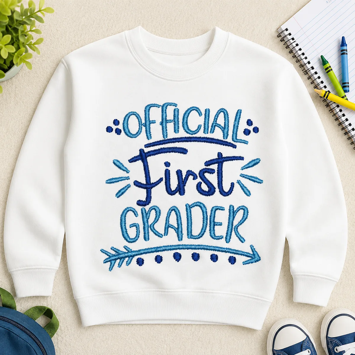 Blue Official First Grader embroidery design stitched on a white kids sweatshirt for first day of school and back-to-school outfits