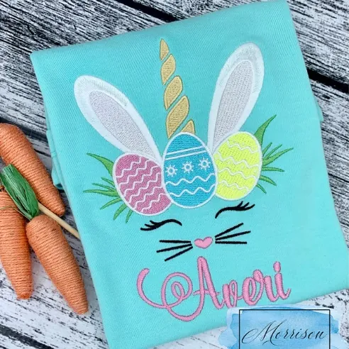 Easter unicorn embroidery design with bunny ears, Easter eggs and the name Averi on a mint shirt