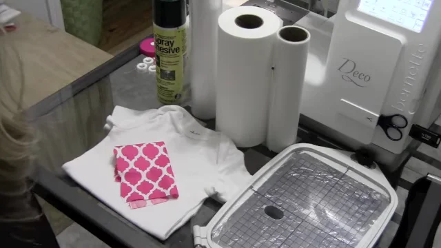 Supplies for embroidering a onesie: baby bodysuit, applique fabric, stabilizer rolls, temporary spray adhesive and embroidery hoop
