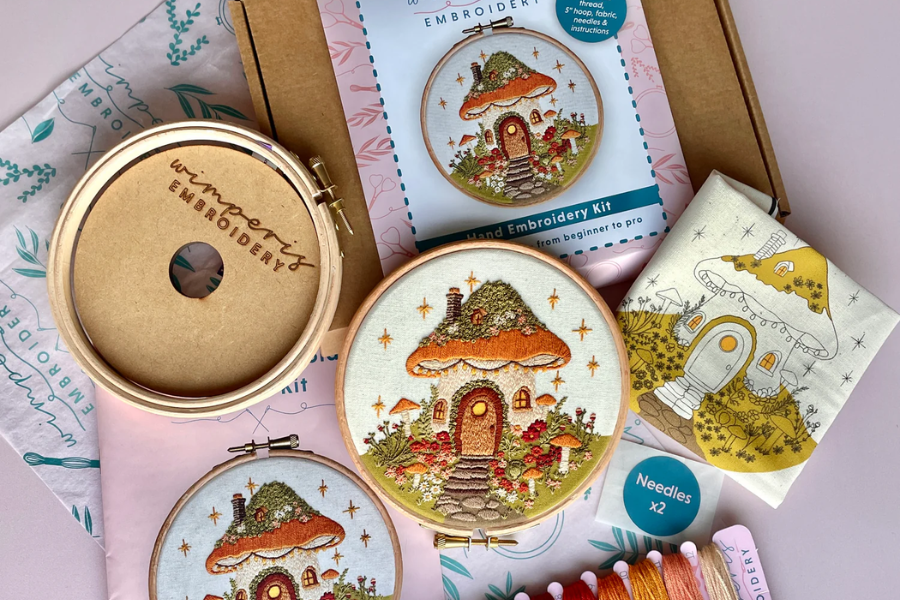 Hand embroidery kit with mushroom house design showing hoop, fabric, needles, and thread for beginner embroidery projects