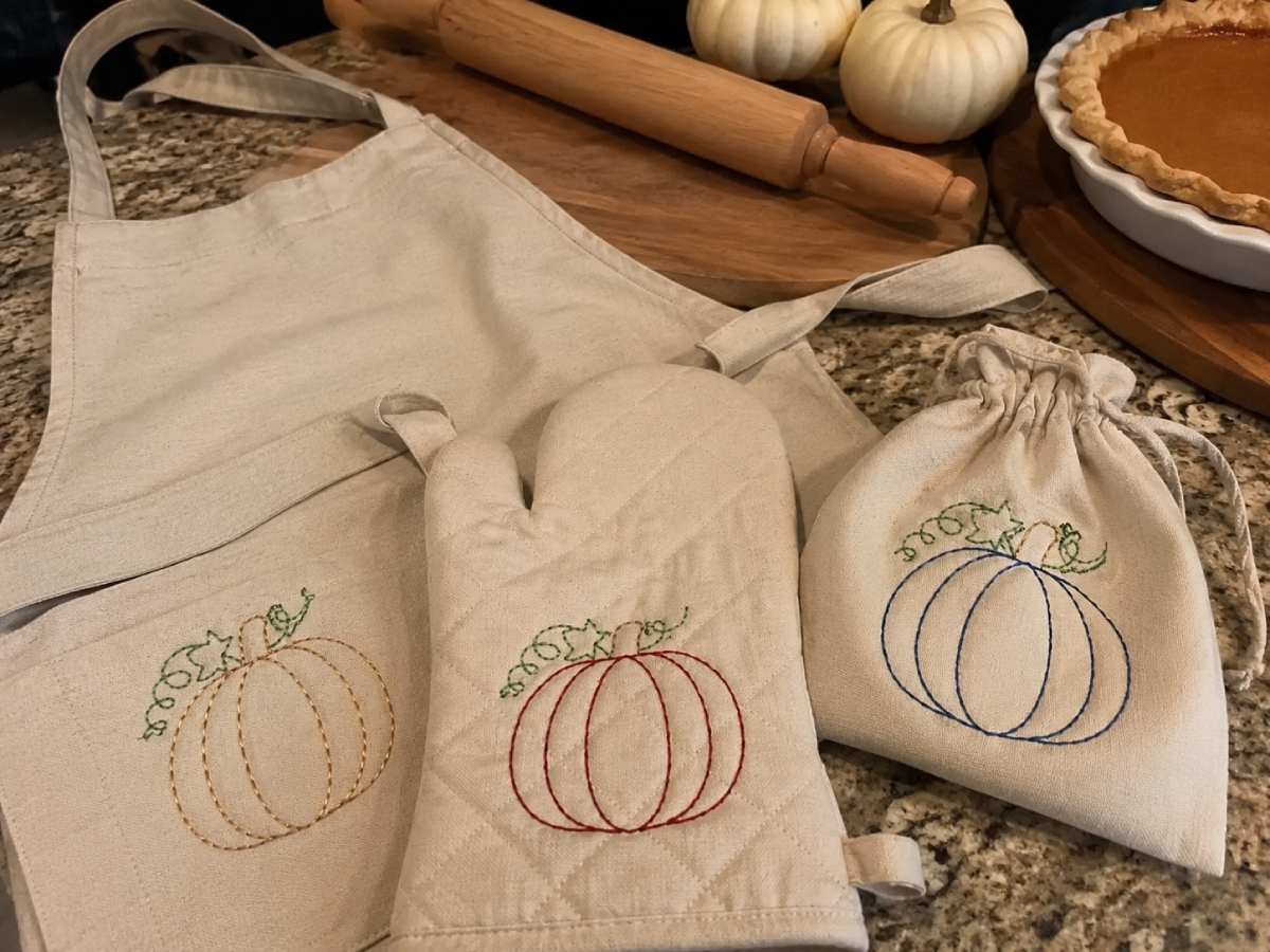 Simple pumpkin embroidery designs on an apron, oven mitt, and gift pouch for cozy fall kitchen projects.