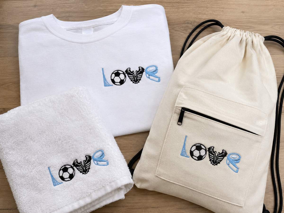The word “LOVE” is built from soccer details: a blue goalpost-style L, a black-and-white soccer ball for the O, black soccer cleats forming the V, and a blue ribbon-style E.
