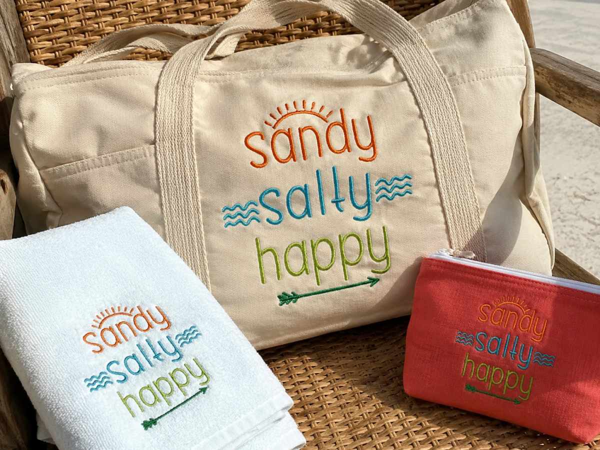 Sandy Salty Happy embroidery brings an easygoing beach mood to towels, totes, and pouches.