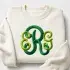 Classic green monogram embroidery design stitched on a folded cream sweatshirt